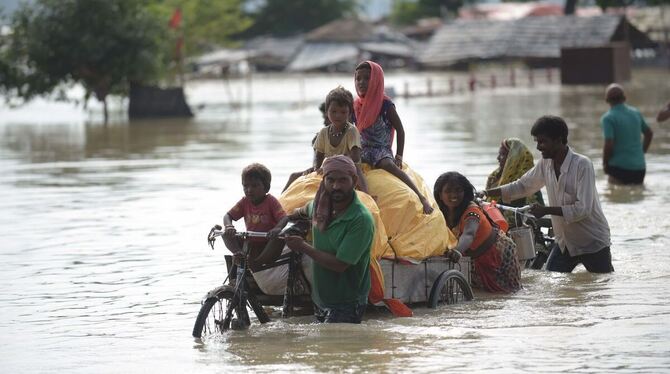 Anwohner waten durch das Hochwasser eines tiefer gelegenen Gebietes am Ufer des Ganges, der während der Monsun-Regen rapide ange