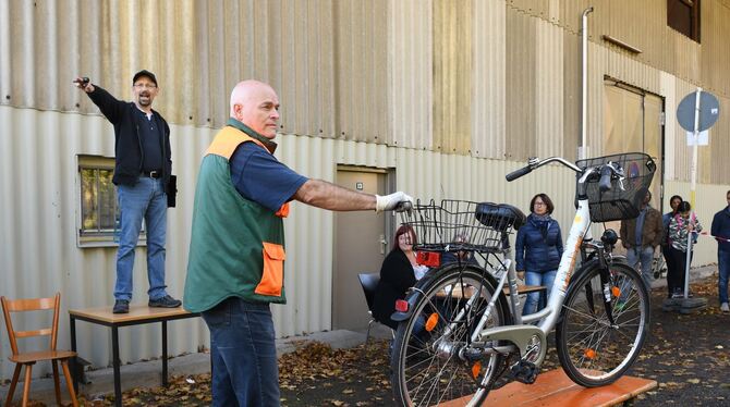 Auktionator Holger Schlosser versteigert stehend auf einem ausrangierten Tisch. Bertram Metzger sorgt dafür, dass die Fahrräder
