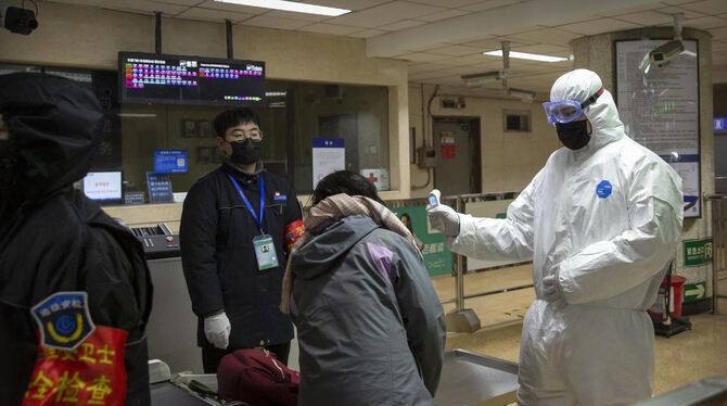 Ein Mitarbeiter trägt in der chinesischen Stadt Paking einen Sicherheitsanzug und überprüft einen Fahrgast in einer U-Bahn-Stati