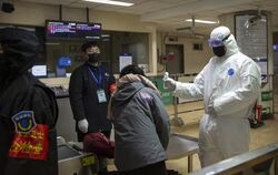 Ein Mitarbeiter trägt in der chinesischen Stadt Paking einen Sicherheitsanzug und überprüft einen Fahrgast in einer U-Bahn-Stati