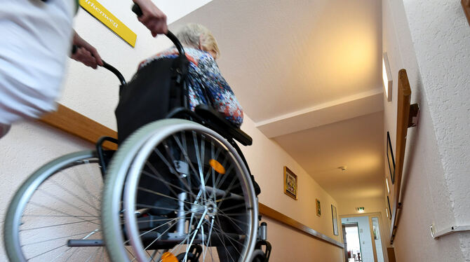 Eine Pflegerin schiebt eine ältere Dame im Rollstuhl über einen Flur in einem Seniorenpflegeheim.  FOTO: DPA