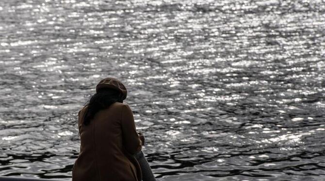 Eine Frau sitzt allein an einem Flussufer Eine Frau sitzt allein an einem Flussufer