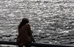 Eine Frau sitzt allein an einem Flussufer