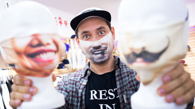 Dominik Klos trägt und zeigt Fotomasken als Mund-Nasen-Schutz in seiner kleinen Textildruckerei in Hamburg-Winterhude. Klos ist