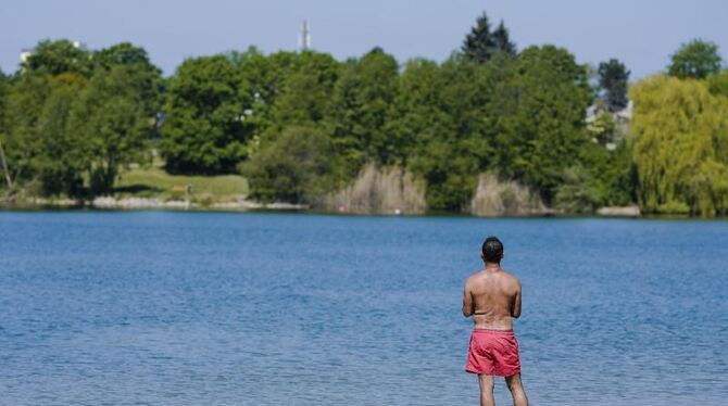 Ein Mann steht am Ufer eines Badesees mit den Füßen im Wasser