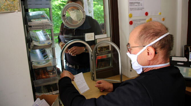 Vorbildlich mit Mund-Nasen-Schutz: Joachim Eissler hinter der Scheibe an der Kasse der Nebelhöhle, die Besucher davor.