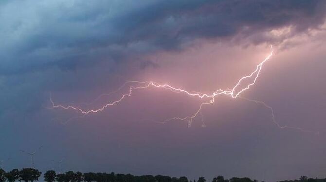 Ein Blitz erhellt den Abendhimmel über einem Feld