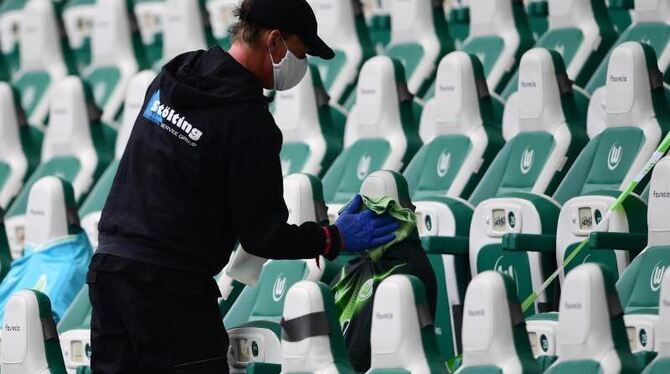 Ein Mitarbeiter desinfiziert die Sitzplätze für Ersatzspieler