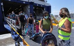 Eine medizinische Mitarbeiterin mit Schutzmaske misst die Körpertemperatur der Passagiere einer Fähre am Hafen. Reisende nach Gr