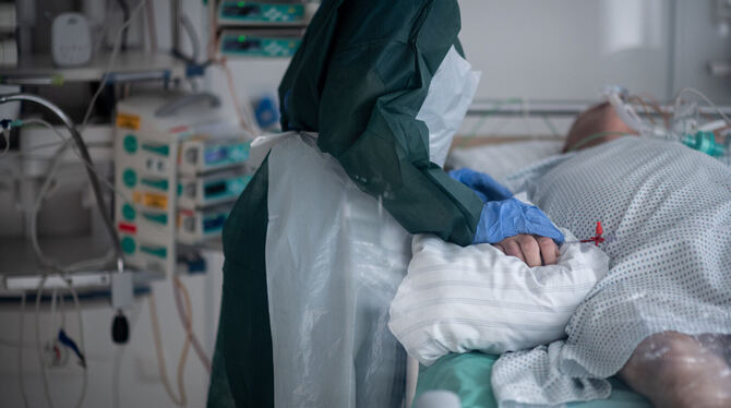 Eine Mitarbeiterin der Pflege in Schutzausrüstung betreut einen Corona-Patienten.   FOTO: STRAUCH/DPA