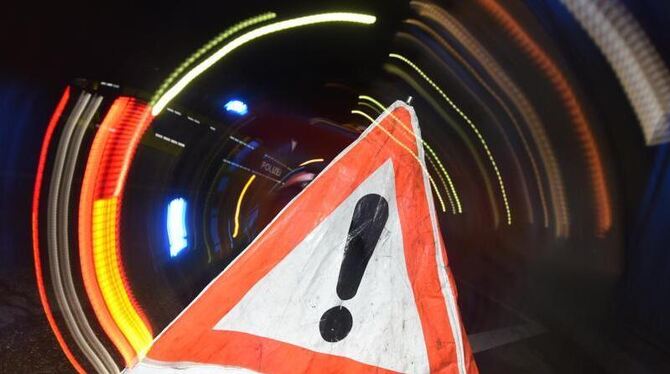 Ein Warndreieck mit dem Schriftzug »Unfall« steht vor einem Blaulicht auf der Straße.