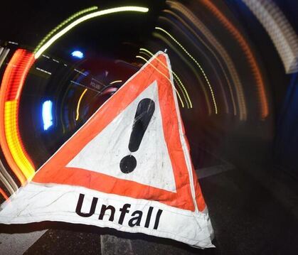 Ein Warndreieck mit dem Schriftzug »Unfall« steht vor einem Blaulicht auf der Straße.