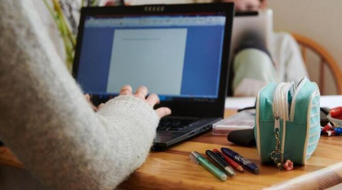 Eine Mutter arbeitet am Küchentisch während ihre Tochter gegenüber in ein Tablet guckt. Eine Mutter arbeitet am Küchentisch während ihre Tochter gegenüber in ein Tablet guckt.