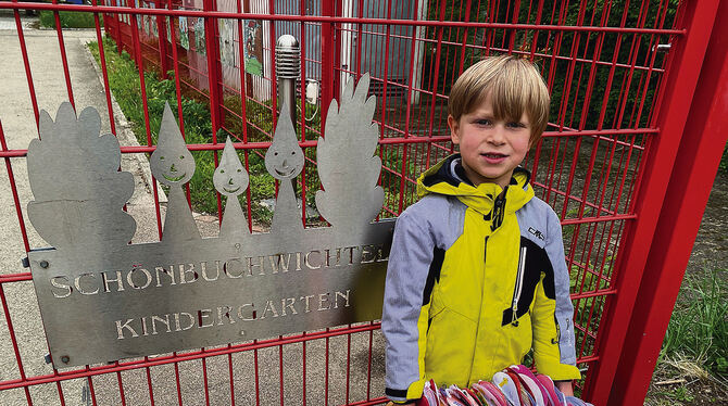 Constantin Ammon steht vor seinem Kindergarten Schönbuchwichtel, in den Händen eine Kiste mit bunt gestalteten, zu einer Kette a
