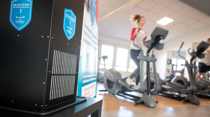 Ein Gerät zur Luftreinigung steht in einem Fitnessstudio vor trainierenden Kunden.