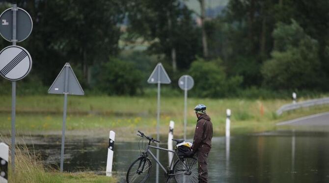 Ein Radfahrer steht an einer überfluteten Straße