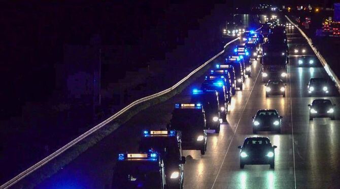 Eine Autokolonne fährt mit Blaulicht über eine Straße