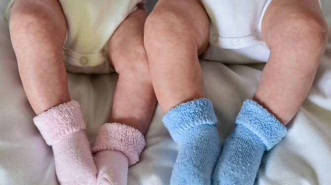 Rosa und blaue Söckchen für ein Mädchen und einen Jungen und die nackten Babybeine von Zwillingen, aufgenommen in einem Babybett