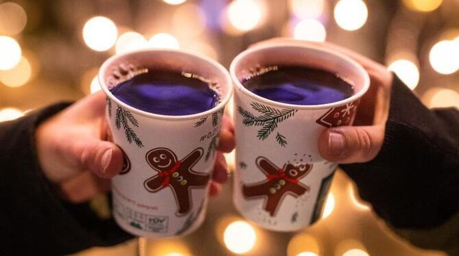 Zwei Besucherinnen eines Weihnachtsmarktes stoßen mit Glühwein an