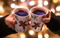 Zwei Besucherinnen eines Weihnachtsmarktes stoßen mit Glühwein an