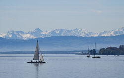 Ein Boot segelt bei Überlingen über den Bodensee, während im Hintergrund die Alpen in der Schweiz zu sehen sind.
