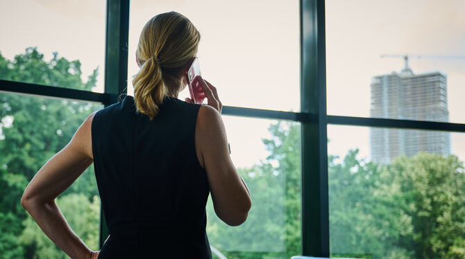Eine Frau steht in einem Büro am Fenster und telefoniert.