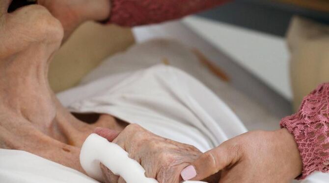 Eine Pflegeschwester hält die Hand einer alten Heimbewohnerin