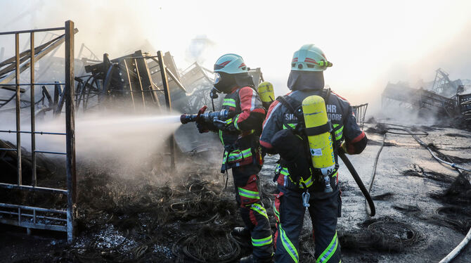 Einsatzkräfte der Feuerwehr stehen während eines Großbrandes auf dem Gelände eines Reifengroßhändlers und löschen das Feuer.