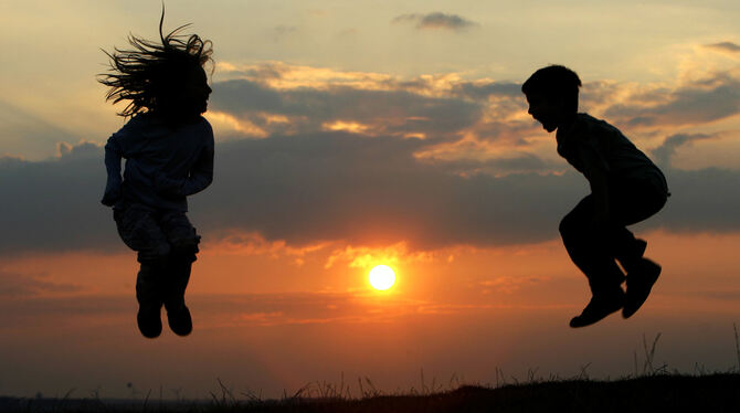 Kinder hüpfen vor dem Hintergrund eines Sonnenuntergangs. Heute ist Weltkindertag, an dem auf die Rechte und Bedürfnisse der Jün