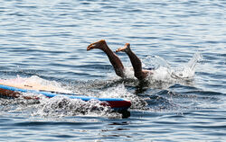 Ein Konstanzer springt von einem Stand-up-Paddle-Board unweit der Uferpromenade in den Bodensee.