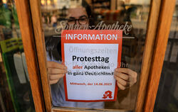 Eine Mitarbeiterin klebt einen Hinweiszettel für den Protesttag an die Tür der Sonnen-Apotheke.  FOTO: WOITAS/DPA 