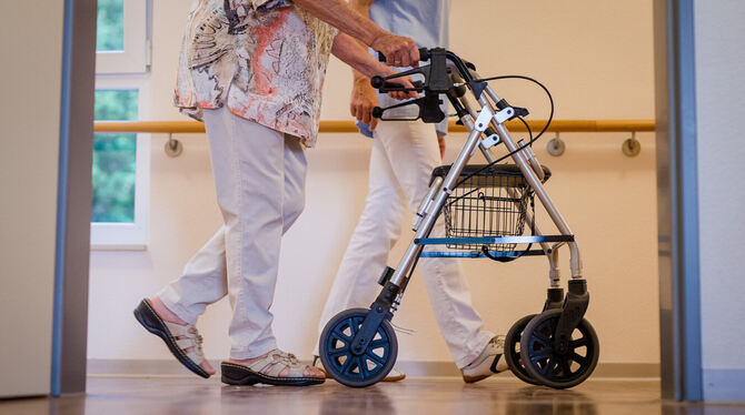 Eine Pflegekraft geht in einem Pflegeheim mit einer älteren Dame über einen Korridor.