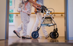  Eine Pflegekraft geht in einem Pflegeheim mit einer älteren Dame über einen Korridor. 