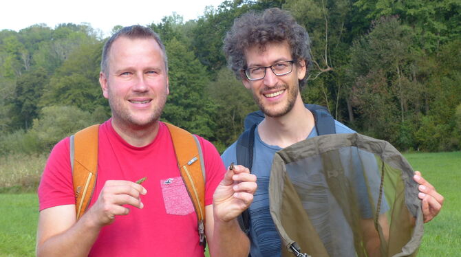 Thomas Bamann (links) mit einer Sumpfschrecke und der Larve einer Feldgrille. Er und Fabian Roser stehen vor einem Feuchtgebiet