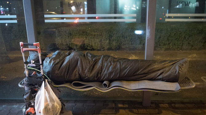 Eingerollt in einen Schlafsack und mit seinen Habseligkeiten auf einer Sackkarre neben ihm stehend, liegt ein Obdachloser in ein