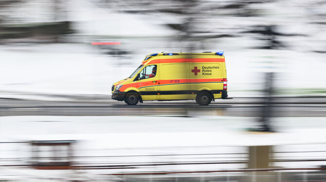 Ein Rettungswagen des Deutschen Roten Kreuzes (DRK) fährt an einer verschneiten Wiese entlang.