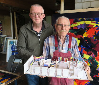 Manfred Efinger und Joachim Wilhelmy vor einer Malerei Lothar Schalls mit einem Modell zum Ausstellungsaufbau.