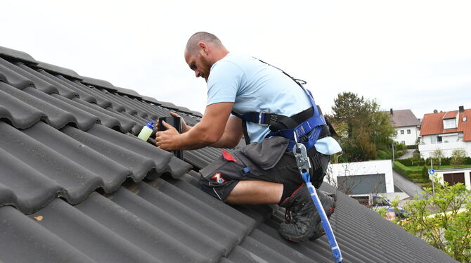 So soll es sein: Mit persönlicher Schutzausrüstung angeseilt arbeitet ein Dachdecker in luftiger Höhe.
