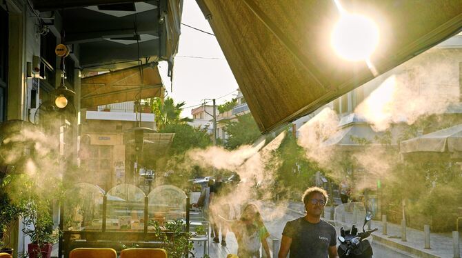 Fußgänger gehen während einer Hitzewelle neben einer Nebelmaschine spazieren. FOTO: GIANNAKOURIS/DPA Fußgänger gehen während einer Hitzewelle neben einer Nebelmaschine spazieren. FOTO: GIANNAKOURIS/DPA
