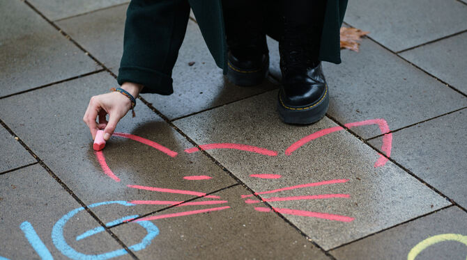 Eine Aktivistin malt mit Kreide ein Katzensymbol neben einen anzüglichen Kommentar aufs Straßenpflaster.