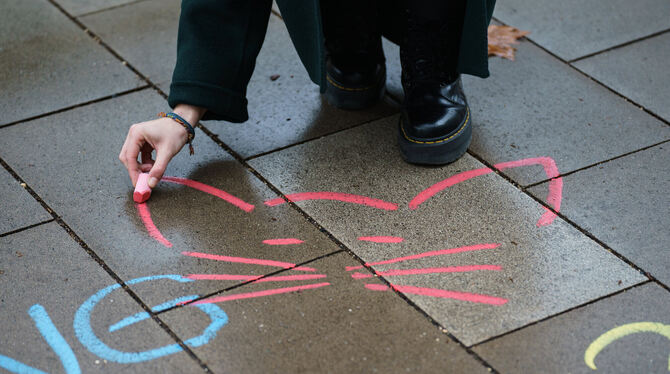 Eine Aktivistin malt mit Kreide ein Katzensymbol neben einen anzüglichen Kommentar aufs Straßenpflaster. Mit diesen Aktionen mac