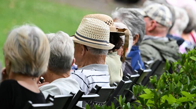 Ältere Menschen besuchen in einem Kurpark das Konzert eines Schulorchesters.