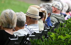 Ältere Menschen besuchen in einem Kurpark das Konzert eines Schulorchesters.
