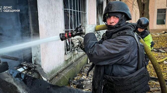 Feuerwehrmänner in Stahlhelmen und Splitterschutzwesten: Ein Bild von Löscharbeiten nach einem Angriff auf ein Werkstattgebäude