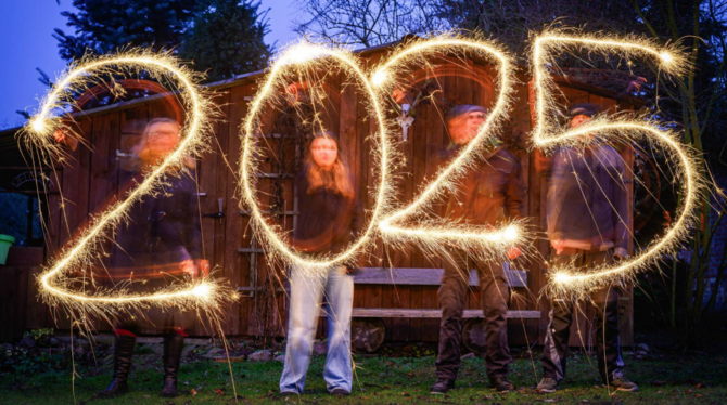 Vier Menschen schreiben mit Wunderkerzen die Jahreszahl 2025 in den Abendhimmel.