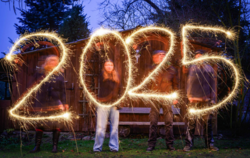 Vier Menschen schreiben mit Wunderkerzen die Jahreszahl 2025 in den Abendhimmel.