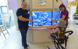 Thomas Musch und Jutta Gaiser stehen mit einer kleinen Patientin beim Meerwasseraquarium im Foyer der Kinderklinik.  FOTO: WEBER