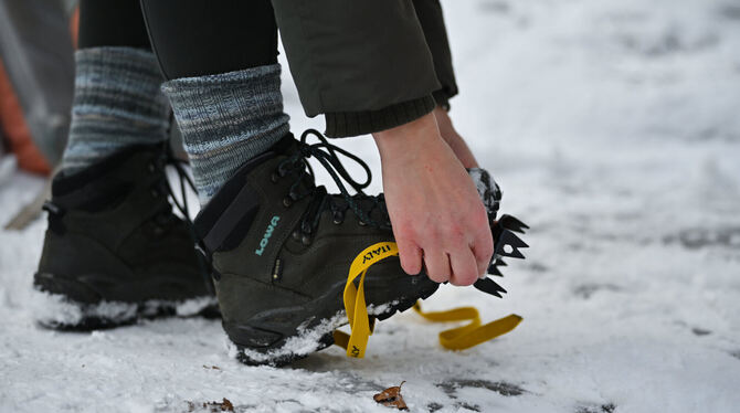 08.01.2026, Baden-Württemberg, Bad Urach: Eine Frau zieht sich am Uracher Wasserfall am Rand der Schwäbischen Alb Spikes an. Fot