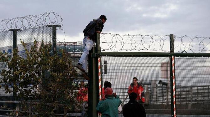 Flüchtlinge klettern über einen Zaun, um einen Zug von Calais nach Dover zu erreichen. Foto: Yoan Valat