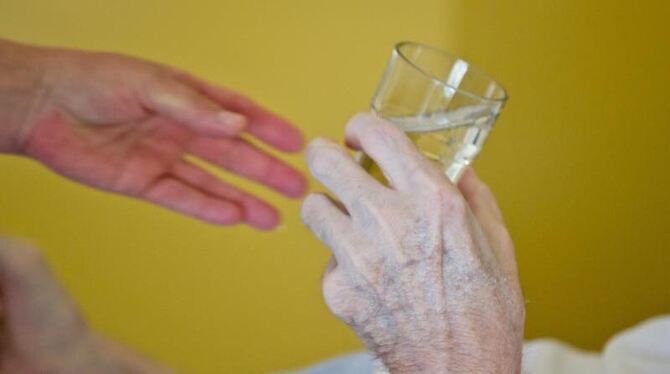 Eine Krankenpflegerin reicht einem Patienten in der Onkologie im Klinikum in Nürnberg ein Glas Wasser. Foto: Daniel Karmann/I